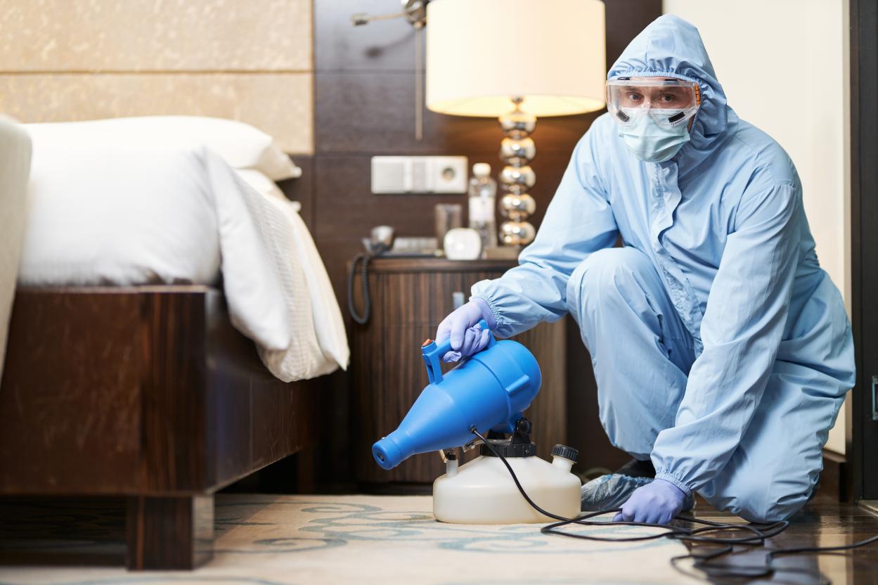 Professional worker in biohazard suit disinfecting